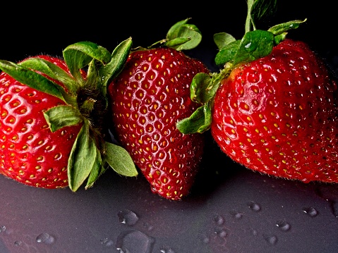 Fresh bright red strawberries with dew drops on a black background. Close-up image with side lighting show the intricate texture and detail of this succulent fruit.