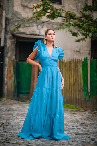 Beautiful young woman walking and exploring old city and wearing blue long dress
