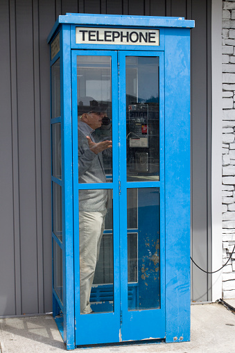 Obsolete run down telephone booth with man inside making a call.