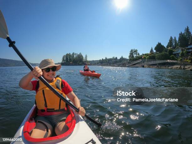 Young Eurasian Woman And Caucasian Man Ocean Kayaking Near Waterfront Homes Stock Photo - Download Image Now