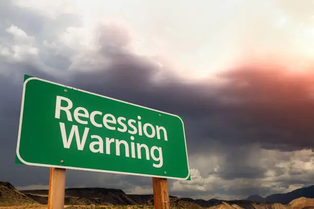 Photo of Recession Warning Green Road Sign Over Dramatic Clouds and Sky.