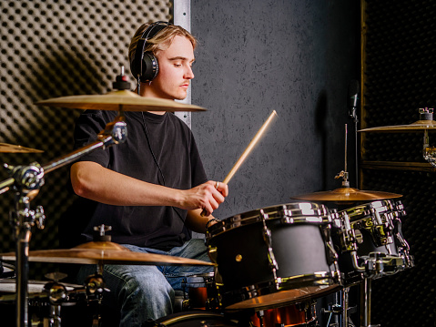 Young man wearing headphones and playing drums in a recording studio.