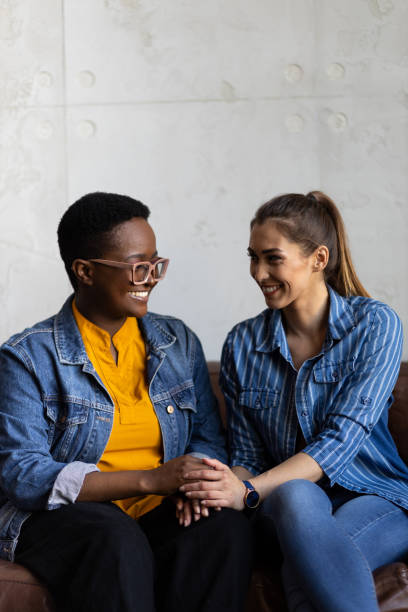 istock Lesbian couple sitting on a leather couch holding hands looking at each other 1394665604
