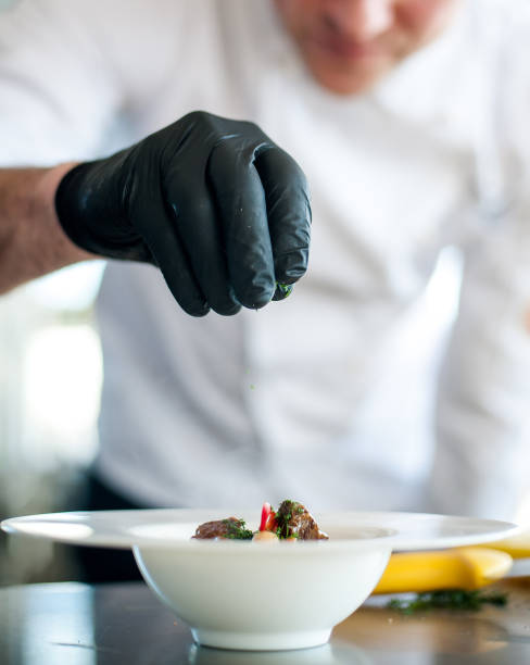 istock The chef prepares the dish. Chef's hand in the frame. Cook on a light background. Cooking. Sprinkles spices on food 1394667264