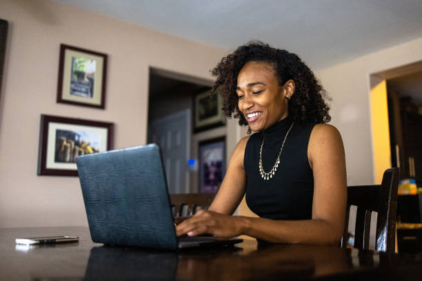 Beautiful Young Black Woman Working at Laptop at Dining Table stock photo