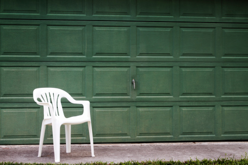 Lonely white chair in front of dark green garage door.