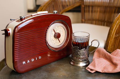 A glass in an antique cup holder with tea and a retro radio are on a copper table against the backdrop of a Victorian-style interior.