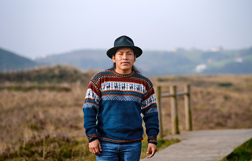 Front view of an indigenous man with traditional sweater and hat in mountains.
