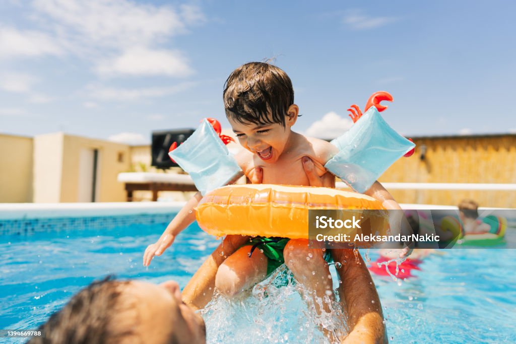Summertime Photo of a little boy having fun with his father while swimming in the pool. Swimming Pool Stock Photo