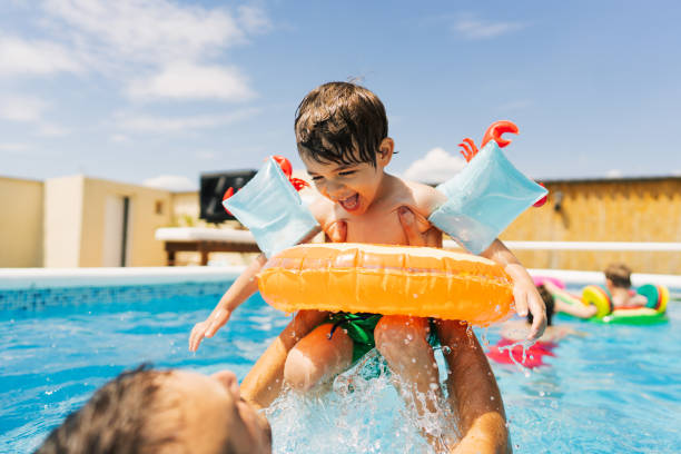 Summertime Photo of a little boy having fun with his father while swimming in the pool. pool party stock pictures, royalty-free photos & images