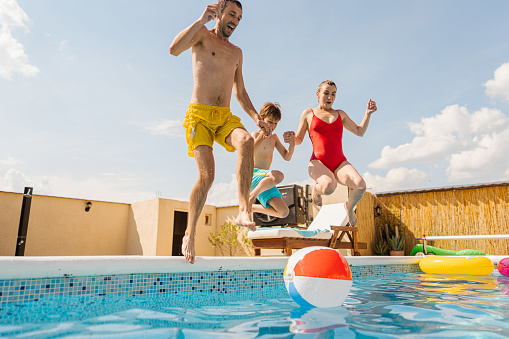 Photo of a family jumping in the swimming pool, having fun and enjoying their summer vacation outdoors.