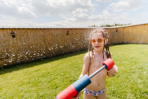 Photo of a little girl having a water fight in the backyard.
