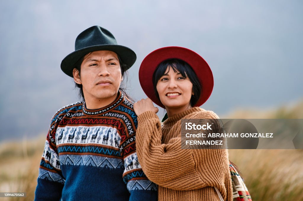 Portrait of indigenous couple dressed in their traditional clothes from their country looking away Portrait of Latin couple dressed in their traditional country clothes and hat looking away with woman leaning on her boyfriend's shoulder in nature. Indigenous Peoples of the Americas Stock Photo