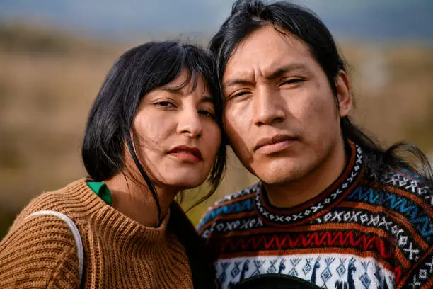 Front view of serious Ecuadorian couple in traditional clothes together looking at camera outdoors. Selective focus.