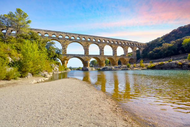 céu colorido no final da tarde ao longo do rio gardon no histórico antigo aqueduto romano pont du gard em vers-pont-du-gard, frança. - aqueduct roman ancient rome pont du gard - fotografias e filmes do acervo