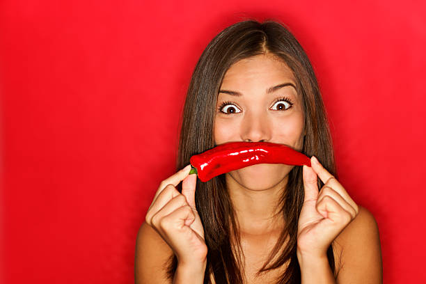 Chili woman funny on red background holding red chili pepper vegetables as mustache looking funny at camera. Beautiful multicultural Caucasian / Chinese Asian girl on red background. See more