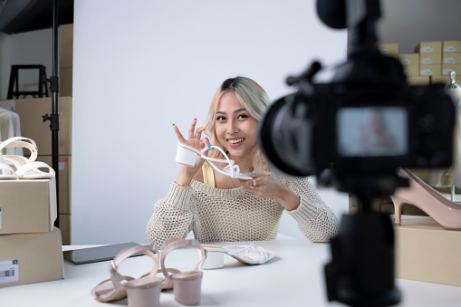 Young attractive Asian female blogger or vlogger looking at camera reviewing product. Modern businesswoman using social media for marketing. Business online influencer on social media concept.