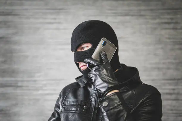 Photo of Robber making phone gesture. concept of telephone terrorism and fraud. A masked man makes a phone call.