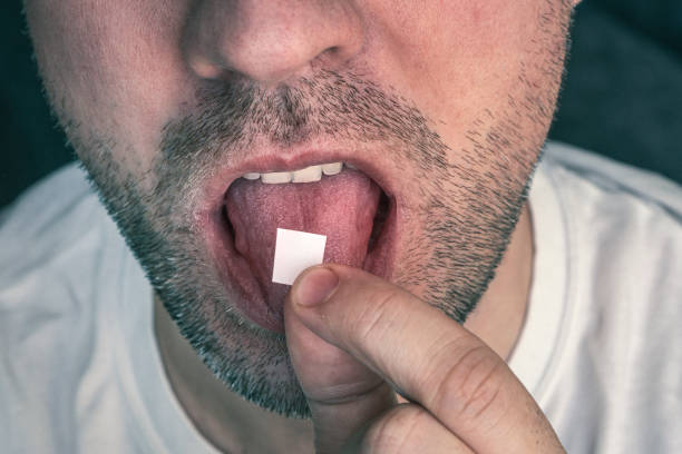 Man with LSD on the tongue On a black background. white stamp with narcotic acid on the tongue. Man with LSD on the tongue. black background. a white stamp with narcotic acid on the tongue. acid stock pictures, royalty-free photos & images