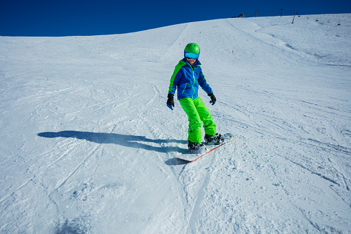 Snowboarder boy go downhill on snowboard fast on the alpine ski slope