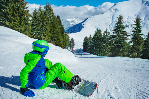 istock Boy sit on the ski track with snowboard attached look downhill 1394711717