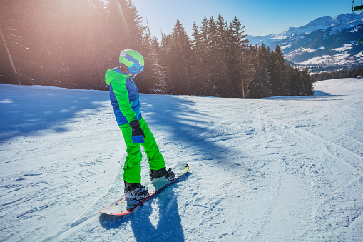 Boy go down ski slope on snowboard from the mountain view from back