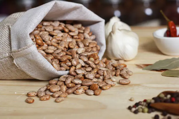 Burlap Sack of Pinto Beans on Table with Spices in Background Shallow DOF