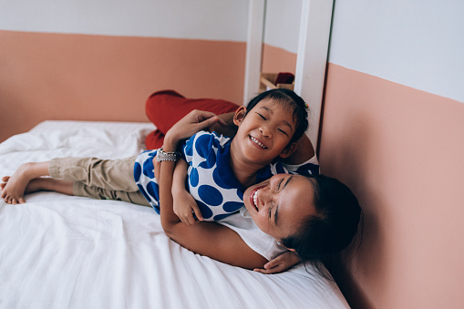 Smiling Thai Mother and Daughter cuddling on the bed.