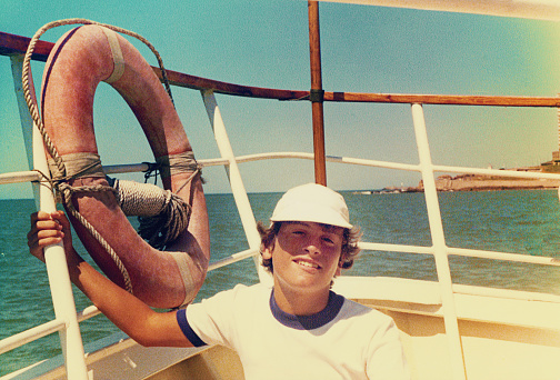 Analog photo of a teenage boy on summer vacation on a boat. Grainy image from the eighties.