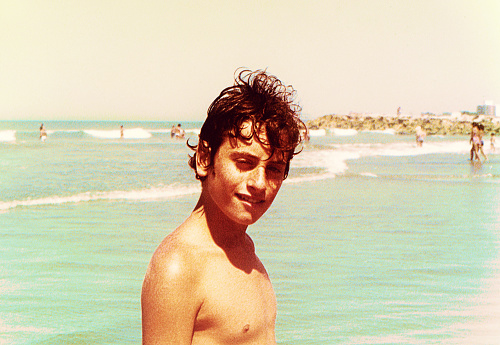 Analog photo of a teenage boy at the beach during summer vacation from the eighties. Grainy image from the eighties.