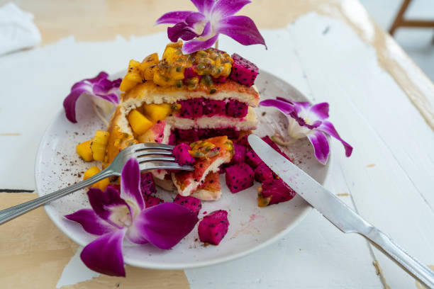 Tasty pancakes with tropical fruits in a plate . Healthy breakfast. Delicious pancakes with mango, dragon fruit and passion fruit, decorated with orchid flowers stock photo