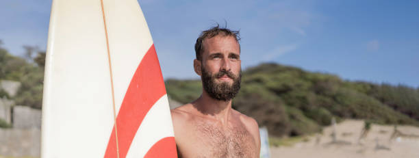 horizontal banner or header with surfer holding his surfboard on the beach - hipster man standing on the beach and waiting big waves for surfing - fit bearded man training with surfboard to sea - hipster people surfing the net internet imagens e fotografias de stock