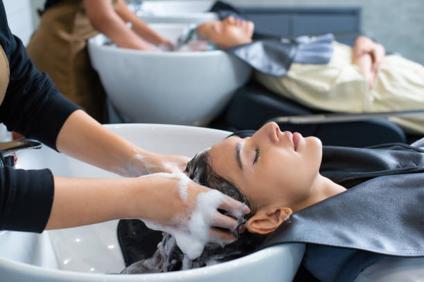 giovane donna nel salone di parrucchiere durante il lavaggio dei capelli dopo il taglio di capelli. donna che applica lo shampoo e massaggia i capelli di un cliente. femmina che si lava i capelli in un salone di parrucchiere. - salone di bellezza foto e immagini stock