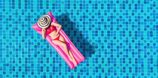 日焼けを楽しむ。休暇のコンセプト。大きなスイミングプールのピンクのエアマットレスにビキニを着てスリムな若い女性のトップビュー。 - bikini summer vacations looking down ストックフォトと画像