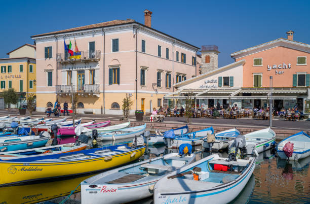 Bardolino, Italy - March 10, 2022:  Boats in the old harbor with the city Hall and restaurants in the backgraund