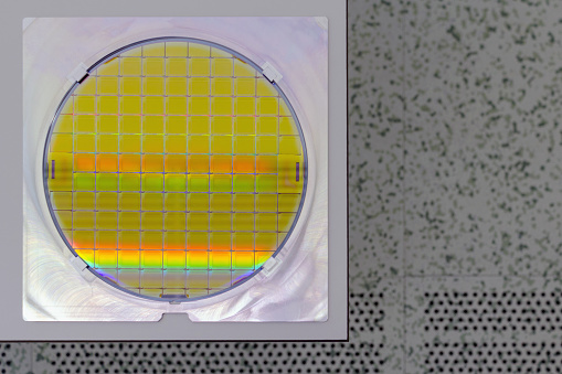 Silicon Wafer in steel holder on a table - A wafer is a thin slice of semiconductor material, such as a crystalline silicon, used in electronics for the fabrication of integrated circuits.Wafer with microchips.Rainbow on silicon wafer.Color silicon wafer with glare.Backside is cleanroom floor.