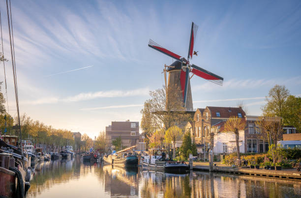 The golden hour in the city of Gouda, the Netherlands. A harbor with boats reflecting in the water and a windmill towering over them. Beautiful sunlight and wispy clouds in the sky. gouda south holland stock pictures, royalty-free photos & images