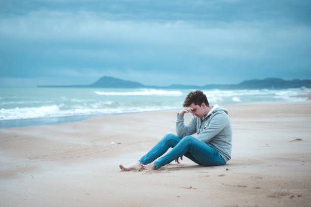 istock Sad Young Man sit on the beach Background 1394738753
