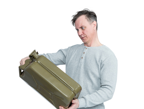 A man holds a green metal gasoline canister in his hands and looks at it, isolated on a white background