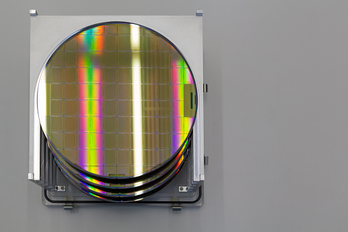 Silicon Wafers in steel holder box on table ,background is grey color- A wafer is a thin slice of semiconductor material, such as a crystalline silicon, used in electronics for the fabrication of integrated circuits.Wafers with microchips.Rainbow on silicon wafers.Color silicon wafers with glare.