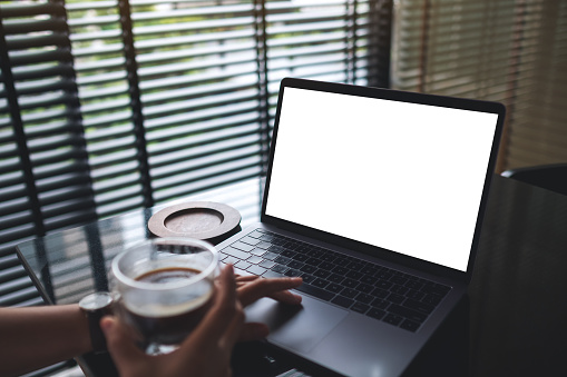 Mockup image of a woman working and typing on laptop with blank white desktop screen while drinking coffee in office
