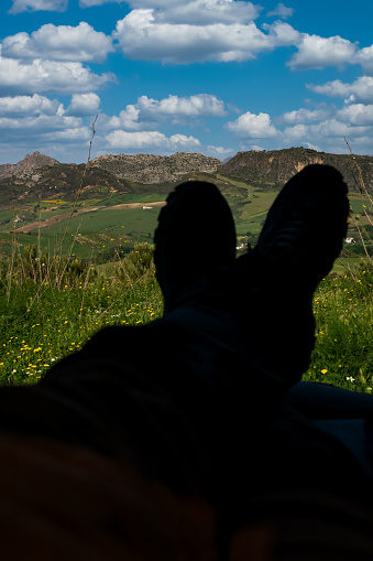 legs of man in shadow lying in his van with cloudy mountain scenery in background
