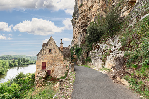 Secluded stone house on road along steep cliff on one side and full-flowing bed of Dordogne river. Dordogne department, New Aquitaine region, France