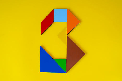 Colorful number three made with tangram toy, teaching counting for children, puzzle toy, colored tangram number 3 isolated on yellow background, side view of third numeric, kids game idea