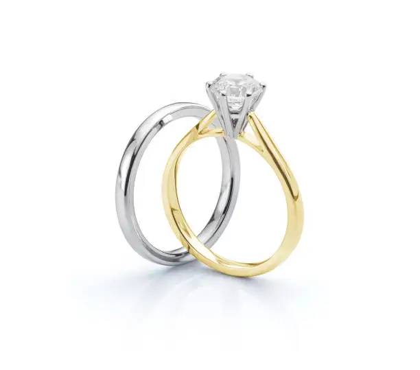 Two ring set comprising a white gold wedding ring with yellow gold solitaire diamond engagement ring isolated on white background.
