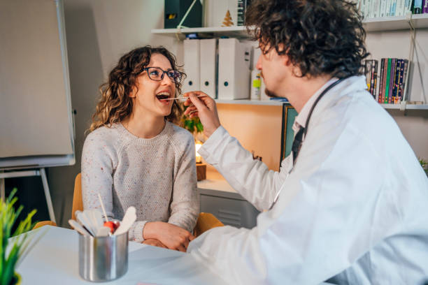 Doctor taking a throat swab Doctor taking a throat swab from the female patient for analysis Saliva stock pictures, royalty-free photos & images