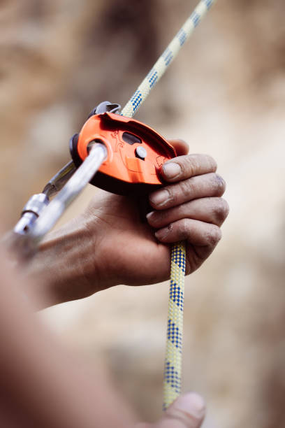 Man's hands operating a rock climbing belaying device Close up shot of a man's hands operating a rock climbing assisted belaying device. safety harness photos stock pictures, royalty-free photos & images