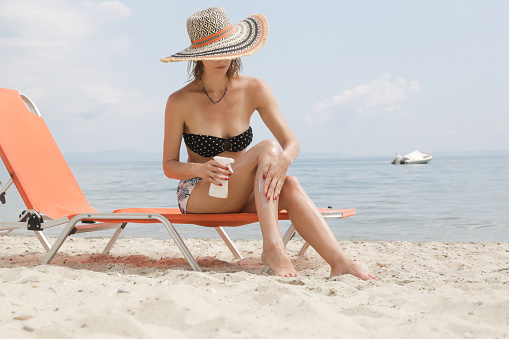 Woman applying sunscreen cream on her legs. Sun protection skin care concept.