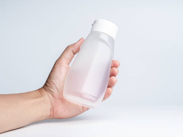 istock Hand holding a white matte plastic bottle curved shape with dispenser for sauces isolated on white background, front view with empty space on it and no label, photo studio shot. 1394753129