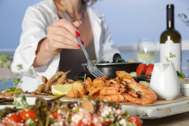 junge frau, die während des sonnenuntergangs im strandrestaurant meeresfrüchteplatte genießt - prepared shellfish stock-fotos und bilder